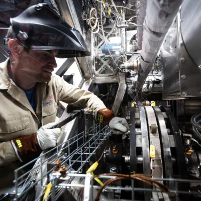 Engineer working on a bunch of tubing and equipment with a welding mask on his head but open visor