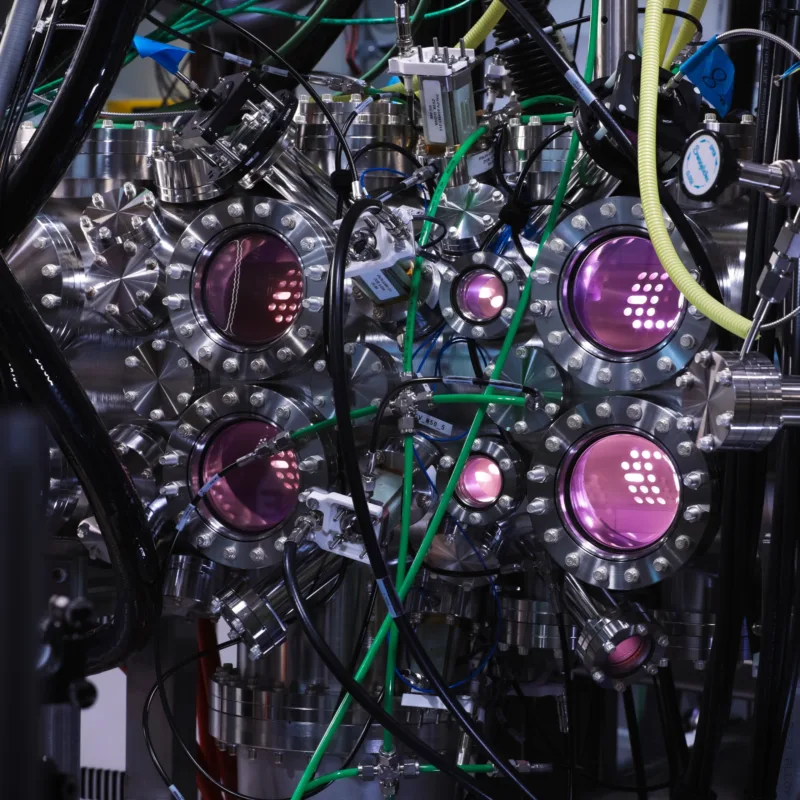 A scientific looking chamber with pink plasma light glowing out of it