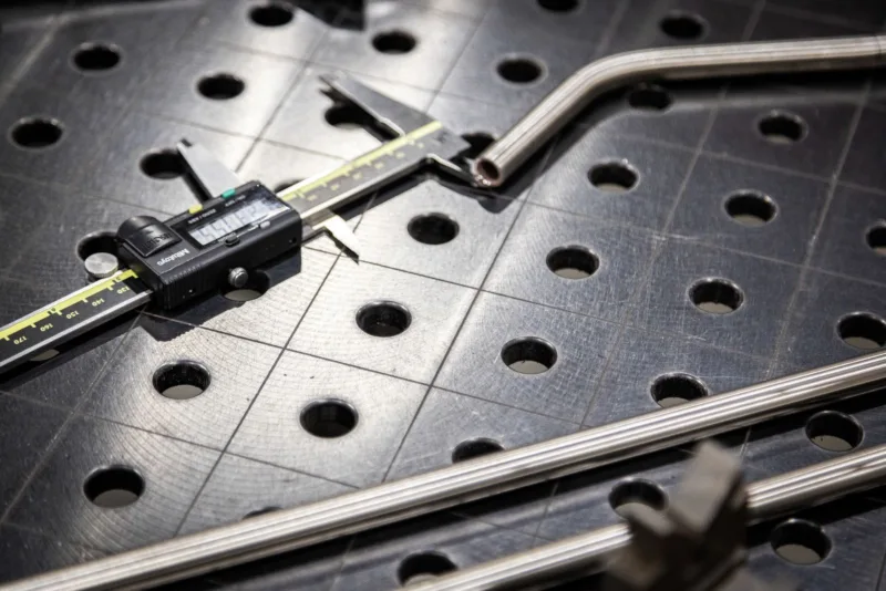metal calipers and metal tubing sit on breadboard in industrial setting