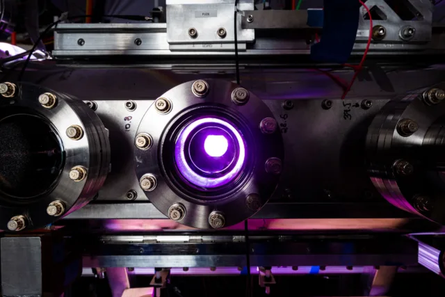 Purple light glows through a window looking into a stainless steel chamber